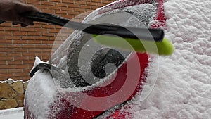 The girl cleans snow on the red car. Action at slow motion.