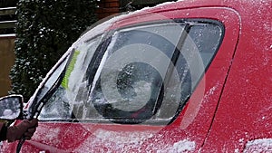 The girl cleans snow on the red car. Action at slow motion. Right side.