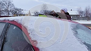 The girl cleans snow on the roof of red car. Winter season at slow motion.