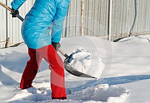 Girl cleans snow shovel on the site near his house. sunlight
