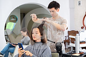 Girl client using phone during hair cut by professional hairdresser