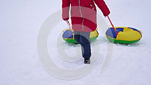 Girl climbs on high snowy mountain holding snow saucer. Children games with sleds in winter. Mountain resort. Christmas