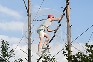 The girl climbs the rope ladder on the climbing wall. Mountaineering in a hike in the woods.