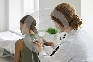 Girl in clinic for a checkup. Doctor with stethoscope examining child& x27;s lungs and heartbeat.