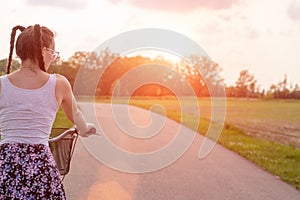 Girl close up with bike at the summer sunset on the road in the city park. Cycling down the street to work at summer sunset.