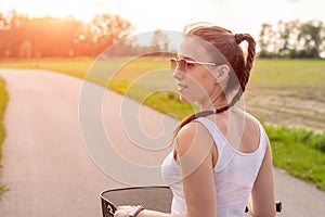 Girl close up with bike at the summer sunset on the road in the city park. Cycling down the street to work at summer sunset.