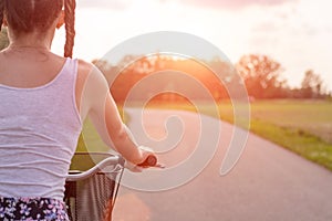 Girl close up with bike at the summer sunset on the road in the city park. Cycling down the street to work at summer sunset.