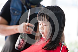 Girl closed eyes on chair at hairdresser. Children cut hair to school. Kids cut the bangs.