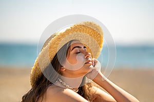 Girl with closed eyes in hat sits on the seashore