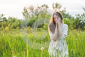 Girl closed her eyes, praying in a field during beautiful sunset. Hands folded in prayer concept for faith