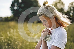 Girl closed her eyes, praying in a field.  Hands folded in prayer concept for faith