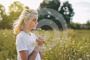 Girl closed her eyes, praying in a field.  Hands folded in prayer concept for faith