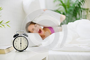 Girl closing ears by pillow to avoid hearing clock