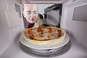 Girl closing her eyes sniffing aroma of pizza cooked in microwave