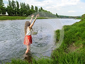 Girl in clothes splashing in Uzh river Uzhhorod, Ukraine - view from the back