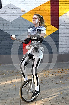 Girl clown rides a unicycle and juggles balls