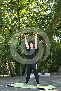 Girl coach performs exercises with dumbbells in the park. Outdoor fitness. Hand training with dumbbells. For beginners