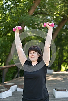 Girl coach performs exercises with dumbbells in the park. Outdoor fitness. Hand training with dumbbells. For beginners. Close up
