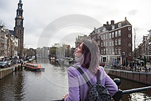 Girl in the coat and backpack enjoying Amsterdam city. Young woman looking to the side on Amsterdam channel