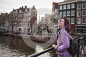 Girl in the coat and backpack enjoying Amsterdam city. Young woman looking to the side on Amsterdam channel