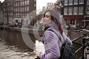 Girl in the coat and backpack enjoying city. Young woman looking to the side on Amsterdam channel, Netherlands