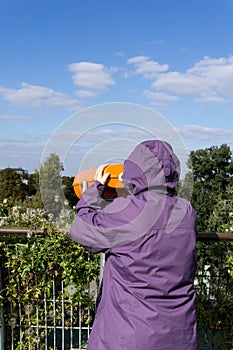 Girl in coat with a hood looking through coin operated binoculars