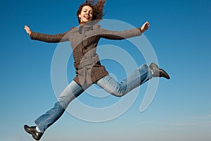 Girl in coat and jeans in jump against blue sky