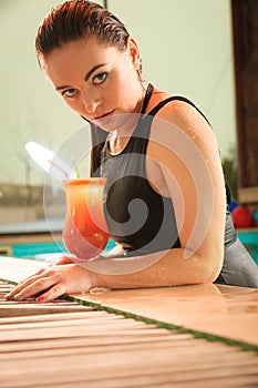 Girl with cocktail drink at swimming pool edge.