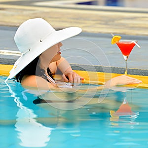 Girl with a cocktail at the edge of the swimming pool