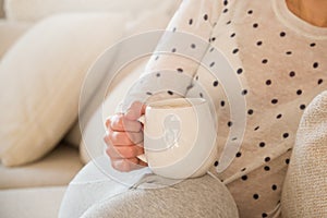 Girl with coffee mug sitting on the sofa indoors. Woman drinking a cup of coffee or tea sitting cozy at home. Relax