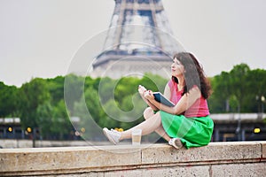 Girl with coffee to go reading a book near the Eiffel tower.