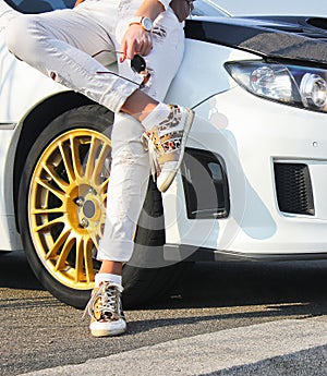 Girl in colored sneakers shoes and in white trousers on background of white car. Girl on car background