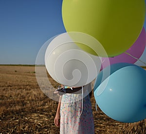 Girl in a field hiding face behind balloons