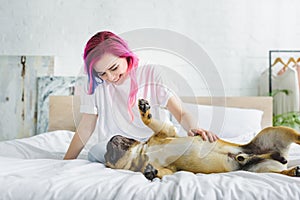 Girl with colorful hair petting and looking at cute french bulldog laying on back