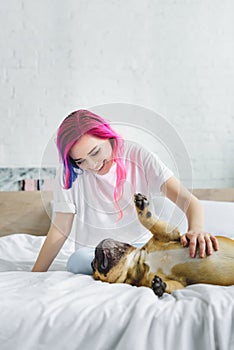 Girl with colorful hair petting and looking at cute french bulldog, which laying