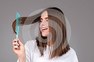 Girl combing hair. Beautiful young woman holding comb straightened hair.