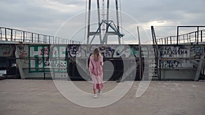 Girl comes to the wall with graffiti at a construction site, unfinished bridge