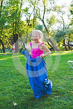 Girl compete in a relay race . Jumping in bags . They laugh and fall .