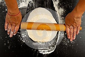 Girl cook rolls the dough for homemade pizza with a wooden rolling pin on a table sprinkled with flour