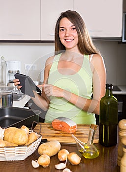 Girl cooking salmon fish and reading ereader