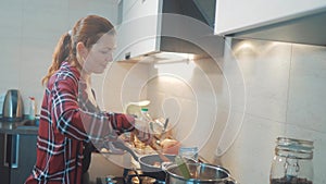 Girl cooks food stands at the stove frying in a griddle stands in the kitchen indoors. woman standing by the stove in