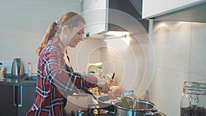 Girl cooks food stands at the stove frying in a griddle stands in the kitchen indoors. woman standing by the stove in