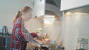 Girl cooks food stands at the stove frying in a griddle stands in the kitchen indoors. woman standing by the stove in