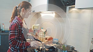 Girl cooks food stands at the stove frying in a griddle stands in the kitchen indoors. woman standing by the stove in