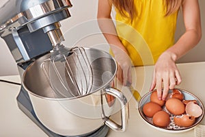 A girl cooks homemade cake in the kitchen, beats eggs in a mixer on the kitchen table. Hands break eggs. Against the