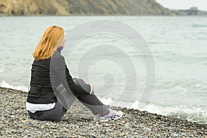 Girl in a cool day sitting on beach and looking thoughtfully into the distance