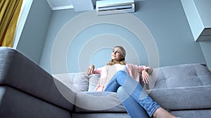 Girl cooling down on hot day sitting on couch under air conditioner, bottom view