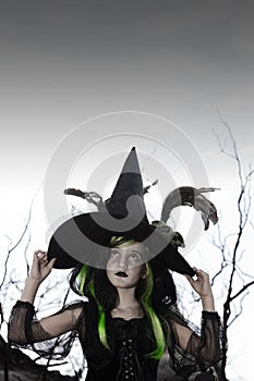 Girl costumed as witch looking up holding her hat