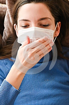 The girl coughs in a bandage. first signs of coronavirus. Girl in a white mask closes her mouth with her hand and coughs close-up