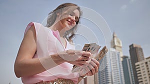 The girl counts in her hands the money of the United Arab Emirates against the background of the city center of Dubai.